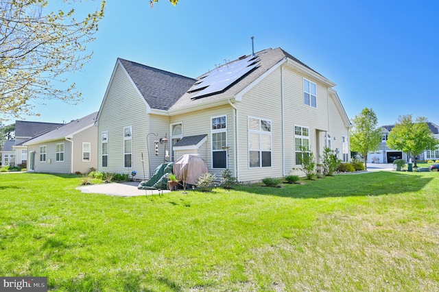 back of property with solar panels and a yard