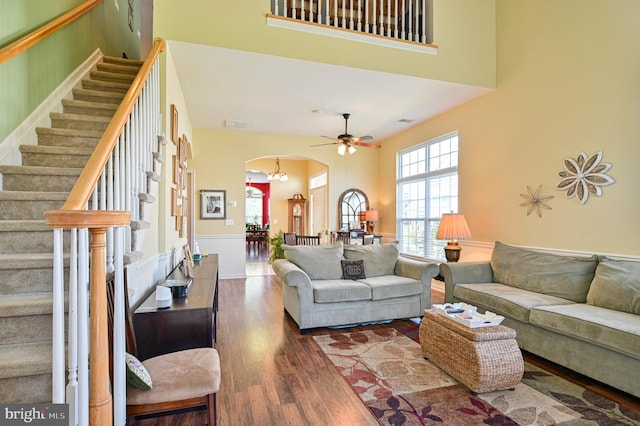 living room with ceiling fan with notable chandelier, dark hardwood / wood-style floors, and a towering ceiling