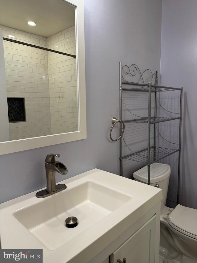 bathroom featuring a tile shower, vanity, and toilet