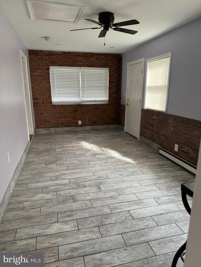 spare room featuring ceiling fan, light wood-type flooring, brick wall, and a baseboard heating unit