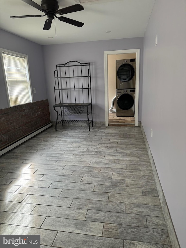 unfurnished room featuring a baseboard heating unit, stacked washing maching and dryer, ceiling fan, and light hardwood / wood-style floors