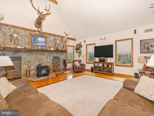 living room with hardwood / wood-style floors, a wood stove, and high vaulted ceiling