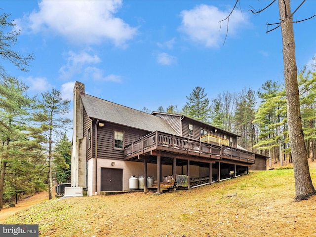 back of property with a wooden deck, a yard, central AC unit, and a garage