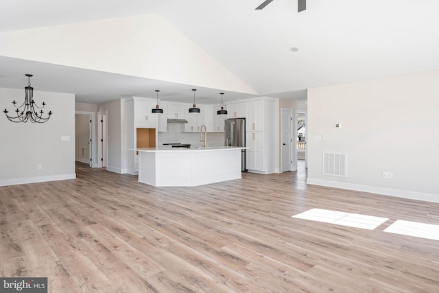 unfurnished living room with ceiling fan with notable chandelier, light hardwood / wood-style floors, high vaulted ceiling, and sink