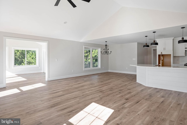 unfurnished living room with plenty of natural light, high vaulted ceiling, ceiling fan with notable chandelier, and light wood-type flooring