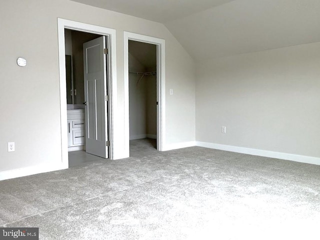 unfurnished bedroom featuring a spacious closet, vaulted ceiling, carpet flooring, and ensuite bathroom