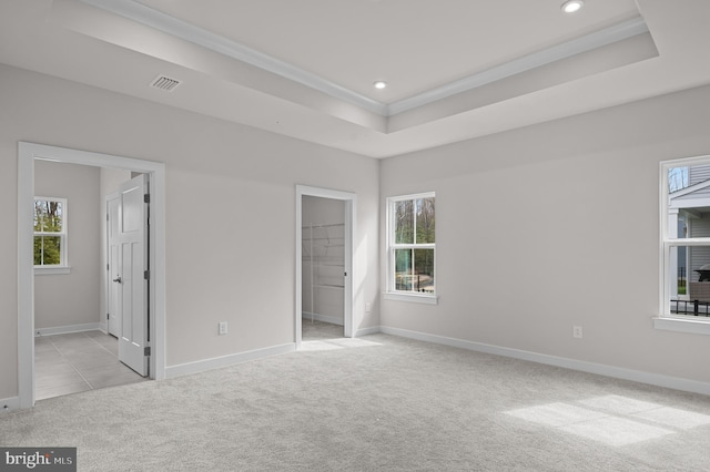 unfurnished bedroom with light carpet, ornamental molding, ensuite bathroom, a tray ceiling, and a walk in closet