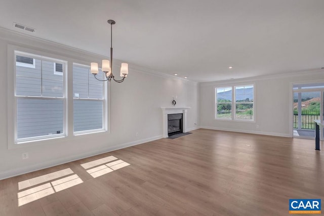 unfurnished living room with light hardwood / wood-style flooring, a notable chandelier, crown molding, and plenty of natural light