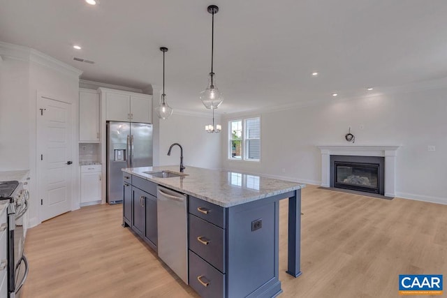 kitchen featuring a center island with sink, white cabinets, hanging light fixtures, sink, and appliances with stainless steel finishes