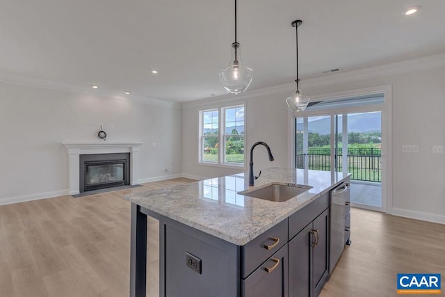 kitchen featuring sink, light stone counters, hanging light fixtures, a kitchen island with sink, and light wood-type flooring