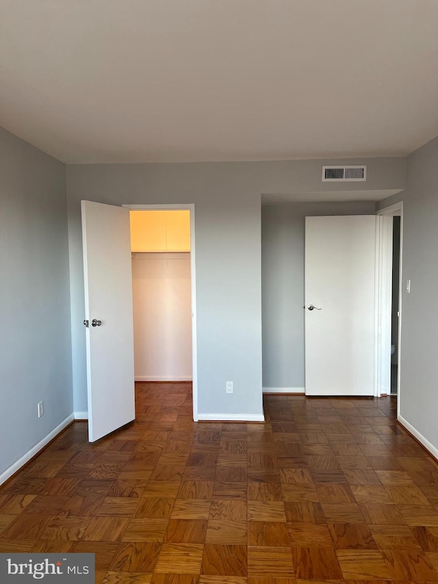 unfurnished bedroom featuring dark parquet floors, a spacious closet, and a closet