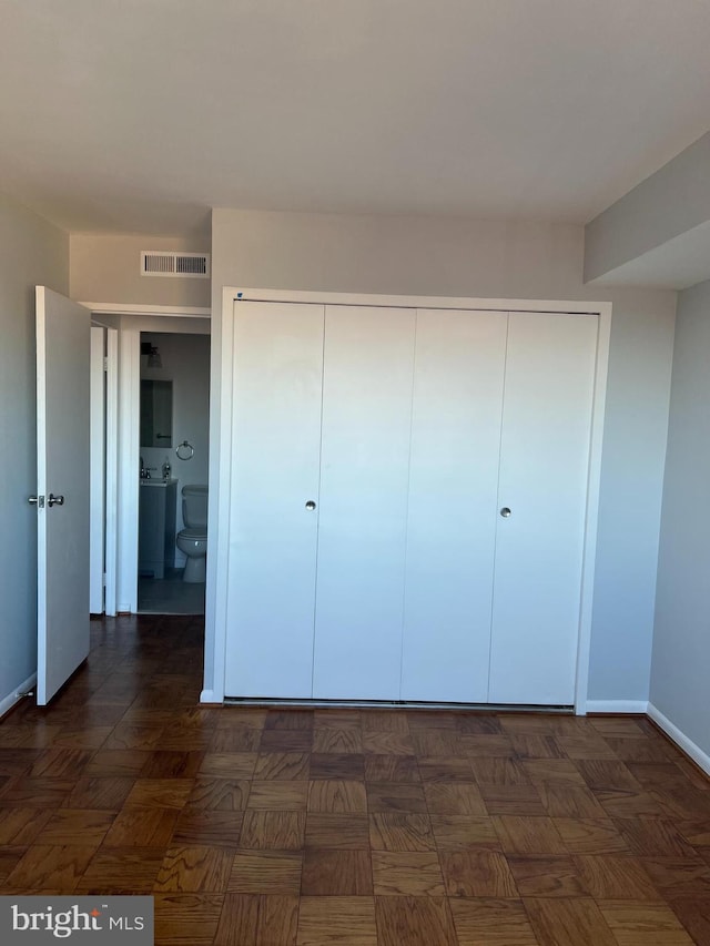 unfurnished bedroom featuring dark parquet flooring, ensuite bathroom, and a closet