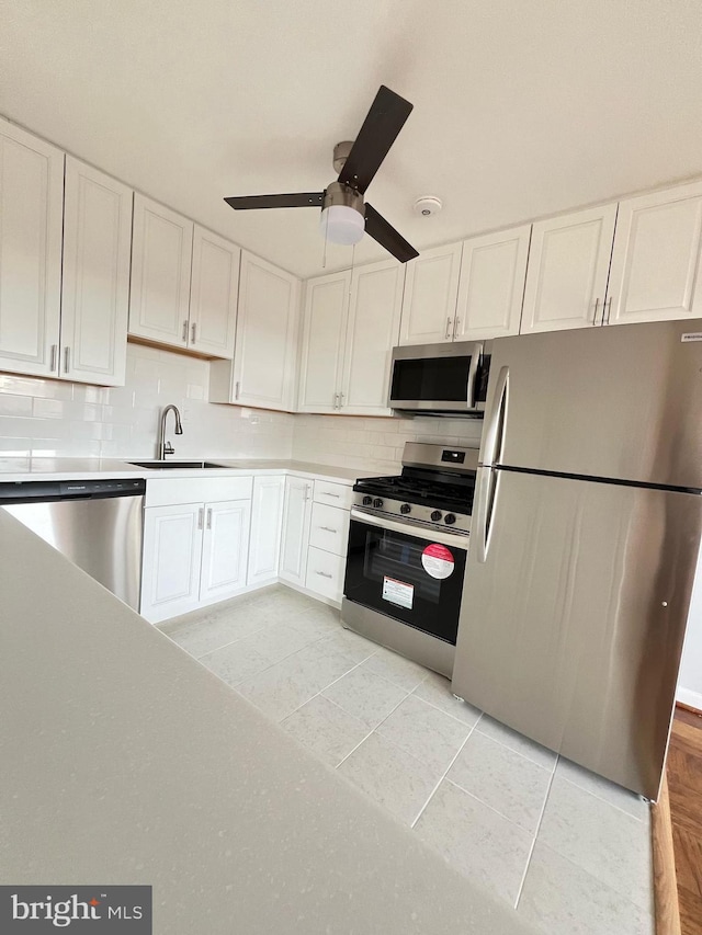 kitchen featuring decorative backsplash, stainless steel appliances, sink, white cabinets, and light tile patterned flooring