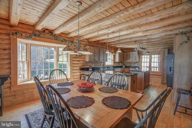 dining space featuring rustic walls, light hardwood / wood-style flooring, beamed ceiling, and a healthy amount of sunlight