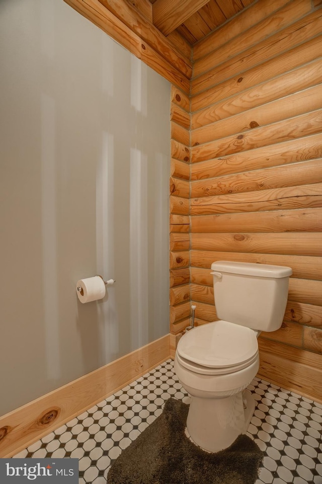 bathroom with toilet, beam ceiling, and log walls