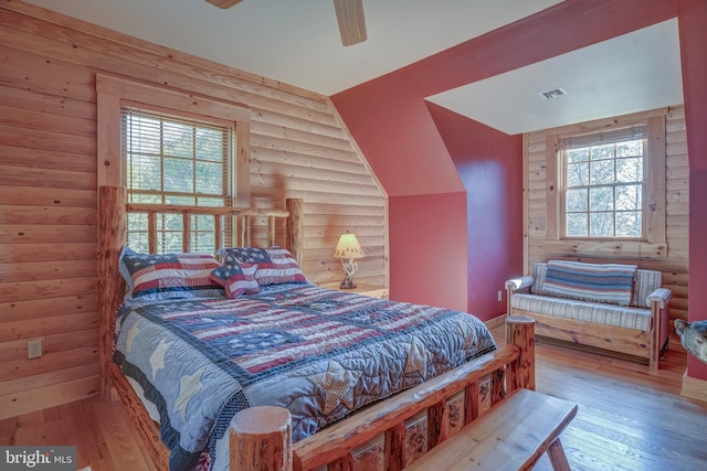 bedroom featuring hardwood / wood-style flooring, ceiling fan, and log walls