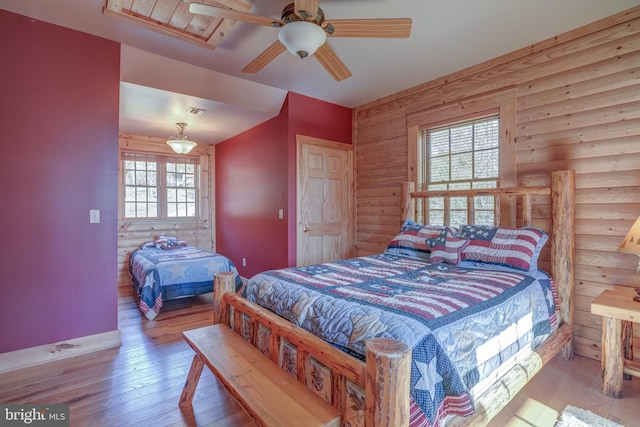 bedroom with ceiling fan, multiple windows, light wood-type flooring, and rustic walls