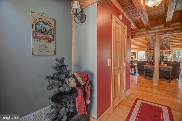 hallway featuring rustic walls, light hardwood / wood-style flooring, beamed ceiling, and wooden ceiling