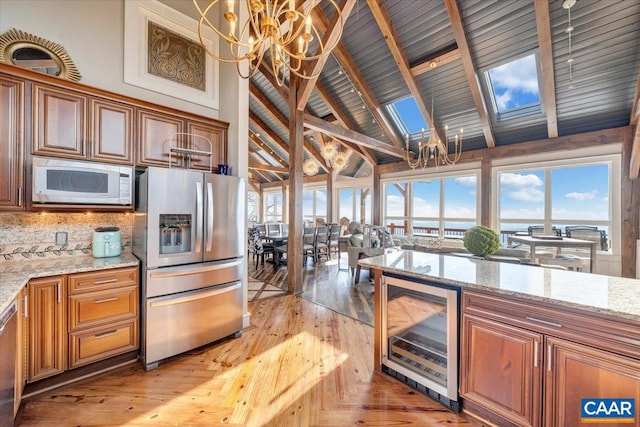 kitchen featuring light stone counters, beverage cooler, stainless steel refrigerator with ice dispenser, high vaulted ceiling, and a skylight