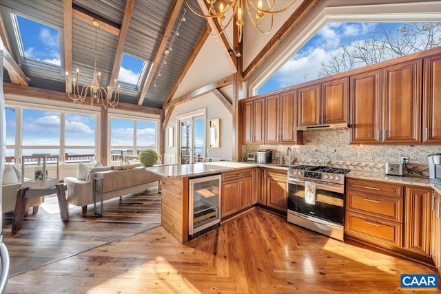 kitchen with beverage cooler, kitchen peninsula, high vaulted ceiling, a skylight, and stainless steel gas range