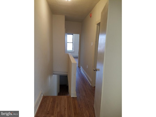 corridor featuring a baseboard heating unit, dark wood-type flooring, and a textured ceiling