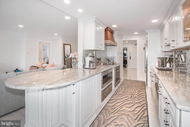 kitchen with white cabinets, custom range hood, and light stone countertops