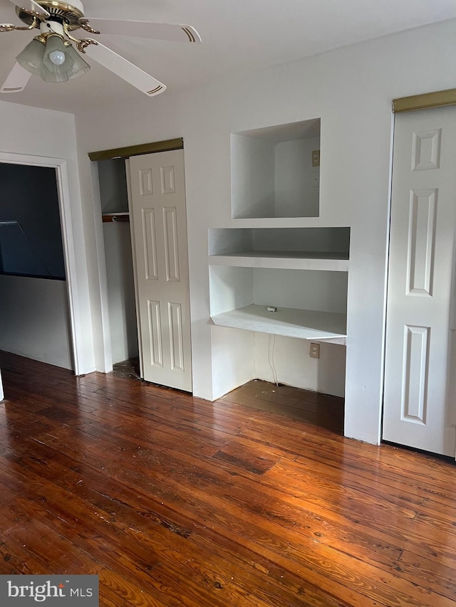 unfurnished bedroom with built in desk, dark hardwood / wood-style floors, and ceiling fan