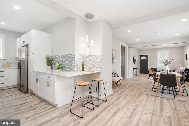 kitchen with white cabinets, stainless steel fridge with ice dispenser, light wood-type flooring, and decorative backsplash