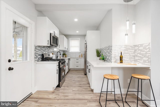 kitchen featuring appliances with stainless steel finishes, backsplash, white cabinetry, and a breakfast bar area