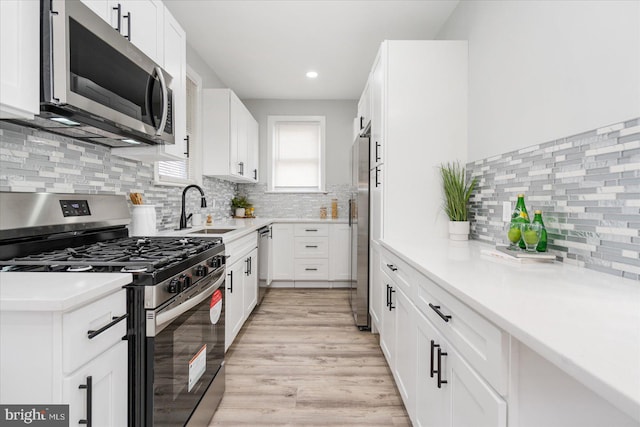 kitchen with white cabinetry, sink, light hardwood / wood-style floors, decorative backsplash, and appliances with stainless steel finishes