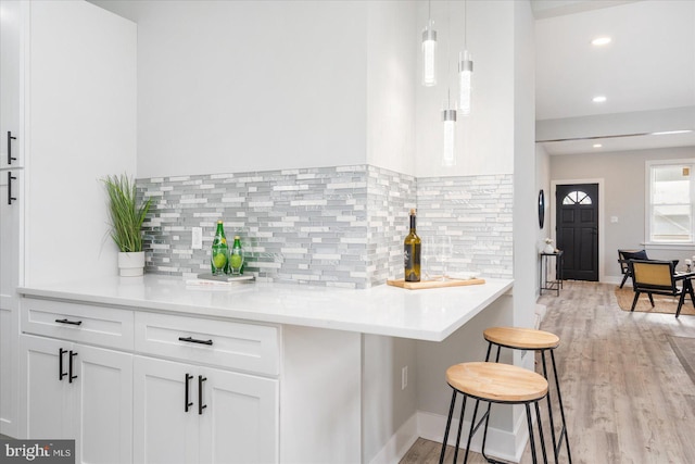 kitchen featuring tasteful backsplash, pendant lighting, light hardwood / wood-style flooring, white cabinets, and a breakfast bar area