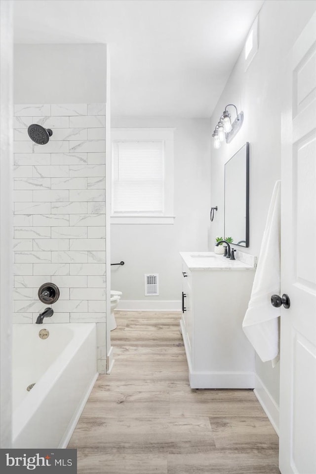 full bathroom with toilet, vanity, wood-type flooring, and tiled shower / bath