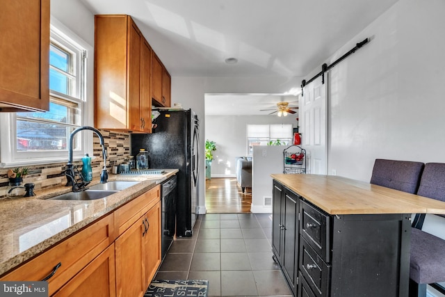 kitchen with black dishwasher, a barn door, tasteful backsplash, and a healthy amount of sunlight