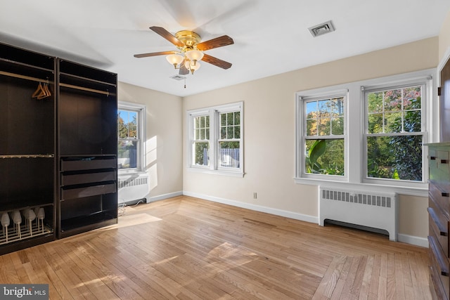 unfurnished living room with light hardwood / wood-style floors, a healthy amount of sunlight, ceiling fan, and radiator