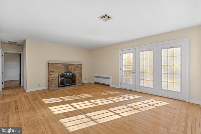 unfurnished living room with radiator, a stone fireplace, light hardwood / wood-style flooring, and french doors