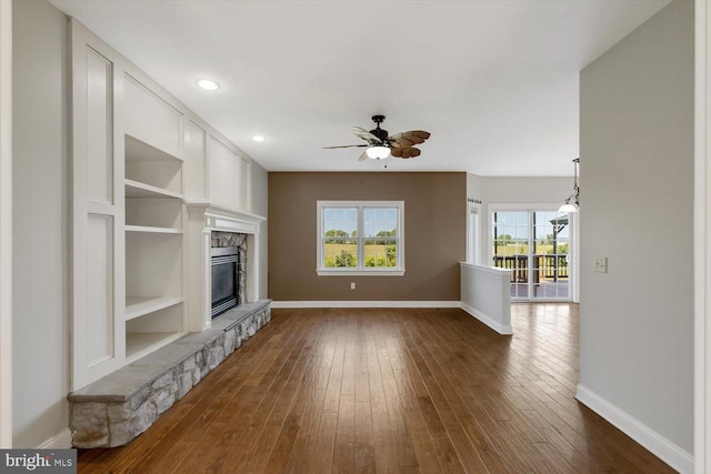 unfurnished living room with dark hardwood / wood-style flooring, built in features, ceiling fan, and a fireplace