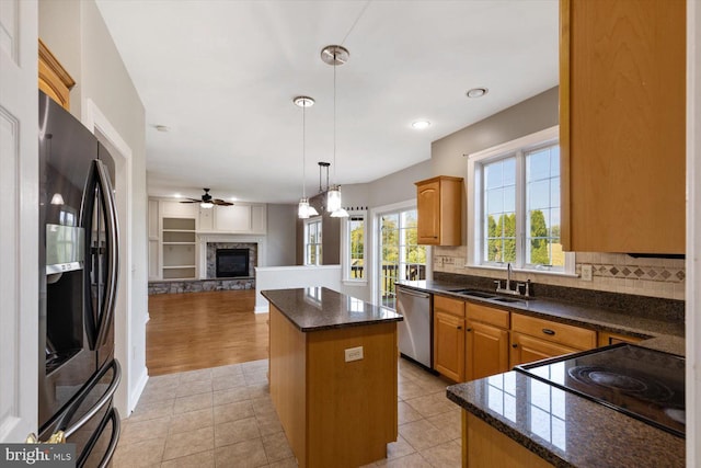 kitchen featuring stainless steel appliances, a stone fireplace, sink, ceiling fan, and a center island