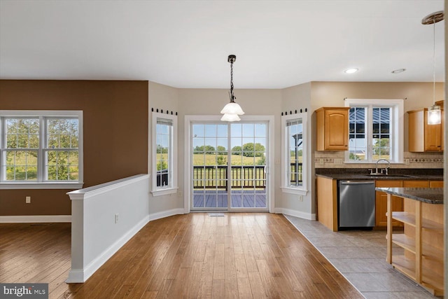 kitchen with sink, decorative light fixtures, backsplash, stainless steel dishwasher, and light hardwood / wood-style flooring