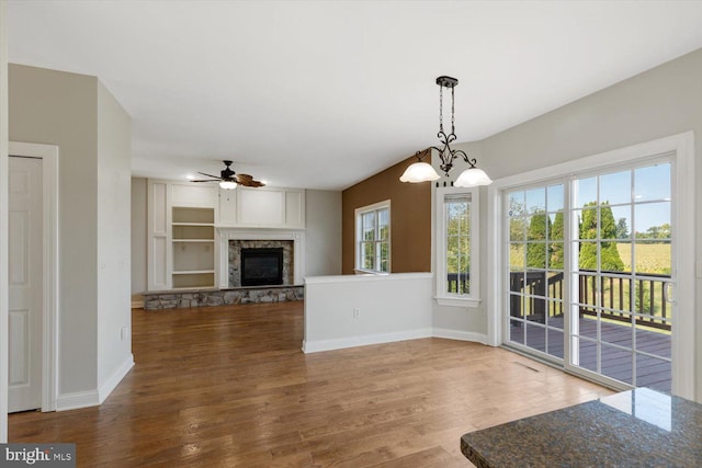 unfurnished living room featuring dark wood-type flooring, ceiling fan with notable chandelier, and a fireplace