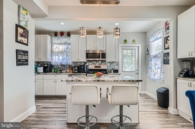 kitchen with stainless steel appliances, white cabinetry, a breakfast bar, hanging light fixtures, and a kitchen island