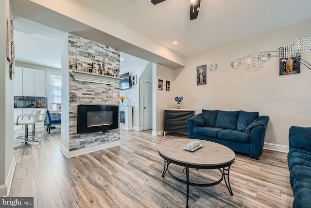 living room featuring a stone fireplace, ceiling fan, and light hardwood / wood-style flooring