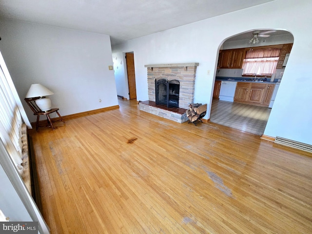 unfurnished living room featuring a fireplace, light hardwood / wood-style flooring, sink, and ceiling fan