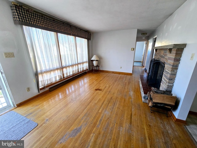 unfurnished living room with baseboard heating, a wealth of natural light, and wood-type flooring