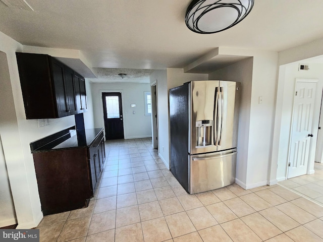kitchen with stainless steel fridge, light tile patterned floors, dark countertops, and baseboards