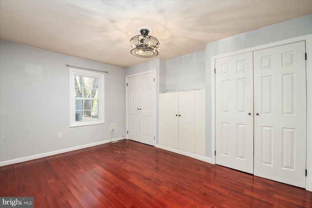 unfurnished bedroom with dark hardwood / wood-style floors, a textured ceiling, a chandelier, and multiple closets