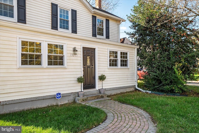 view of exterior entry featuring a chimney and a yard