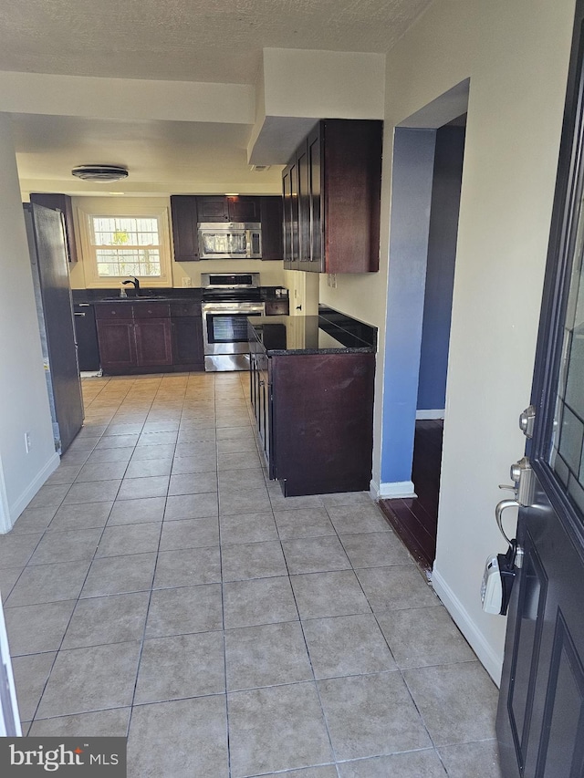 kitchen with stainless steel appliances, light tile patterned flooring, a textured ceiling, and baseboards