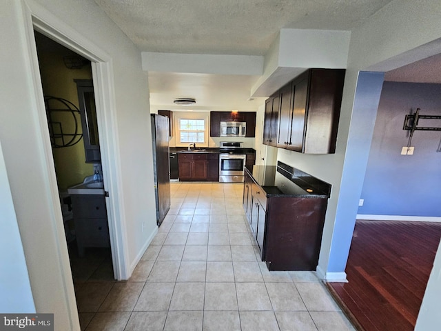 kitchen featuring stainless steel appliances, dark countertops, a sink, dark brown cabinetry, and light tile patterned flooring