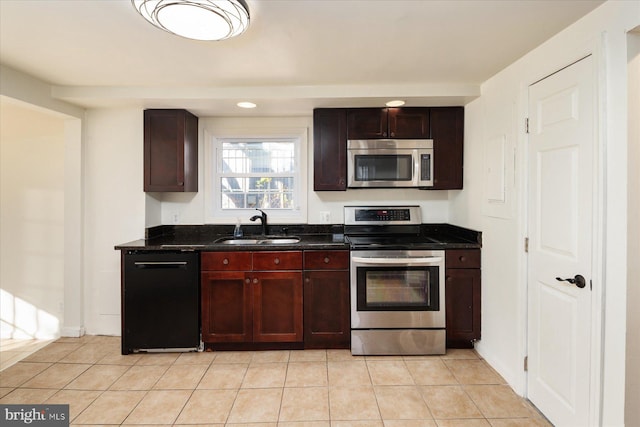 kitchen with appliances with stainless steel finishes, a sink, light tile patterned flooring, and dark stone counters