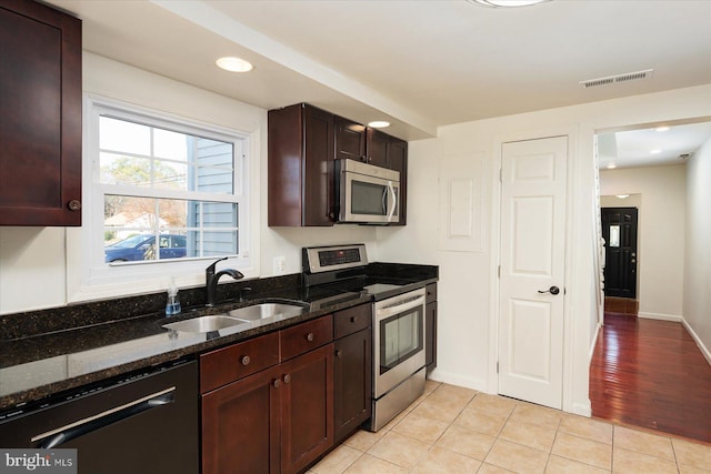 kitchen featuring stainless steel appliances, a sink, dark stone countertops, light tile patterned floors, and dark brown cabinets